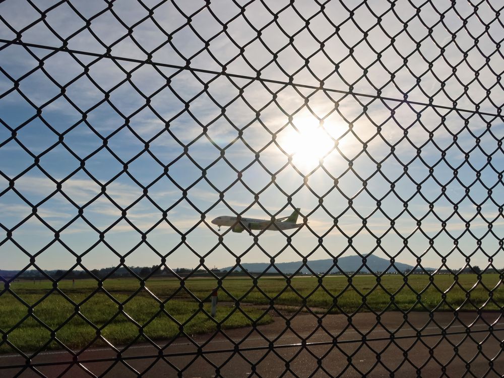 Sonne und Flugzeug hinterm Flughafenzaun